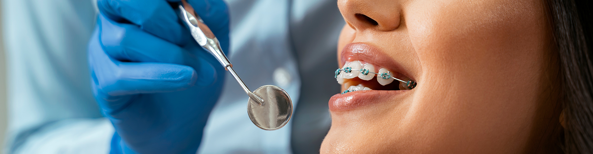 Gloved hand holding mirror near smiling woman with braces.
